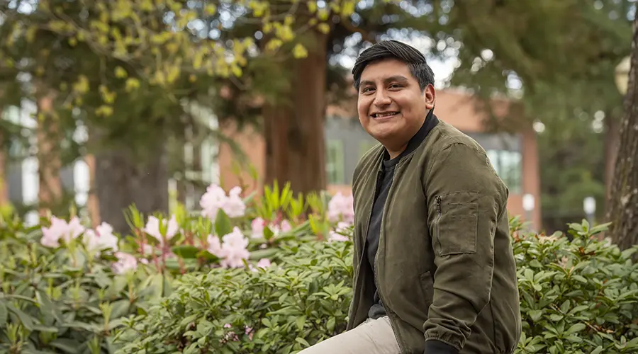 photo of Ivan sitting on a brick wall on the Linfield campus.