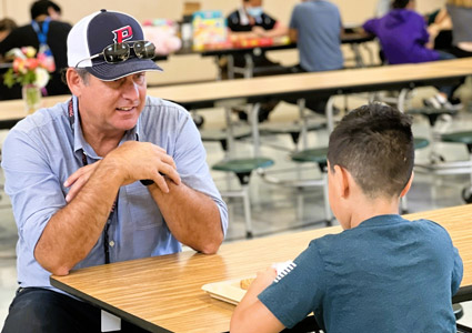 Brent Barry '96 sitting at a cafeteria table with a young student.