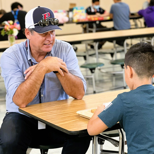 Brent Barry '96 sitting at a cafeteria table with a young student.