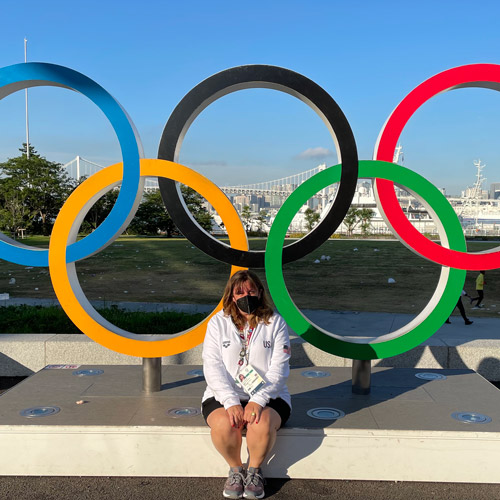 Stacey sitting in front of a five-Olympic ring figure in Tokyo