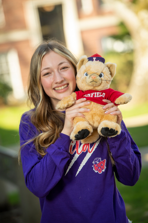 Female student proudly wearing a Linfield t-shirt and holding a Linfield cat stuffed animal.