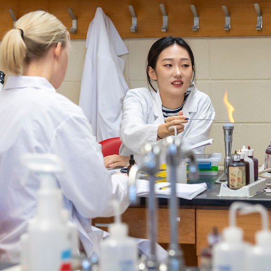 Two female students in white lab coats working in a science lab.