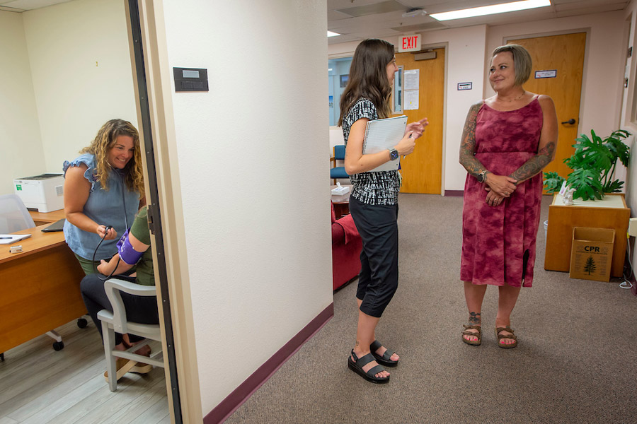 Student health employees talking in the lobby and one employee with a patient in an exam room.