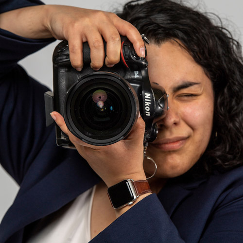 Female JAMS student behind a camera ready to take a photo. 